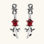 Gothic dangle earrings featuring silver serpent hooks with red enamel roses and metallic stems on white background.