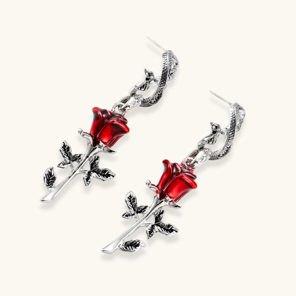 Gothic dangle earrings featuring silver serpent hooks with red enamel roses and metallic stems on white background.