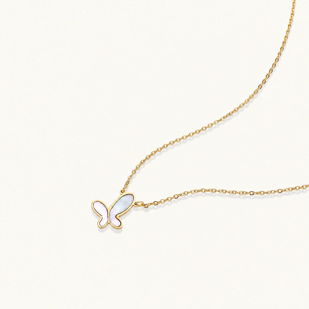 Gold-plated butterfly pendant with iridescent mother of pearl inlay on delicate chain against cream background.