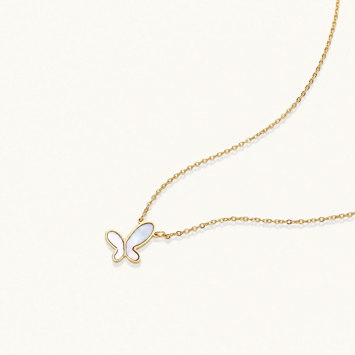 Gold-plated butterfly pendant with iridescent mother of pearl inlay on delicate chain against cream background.