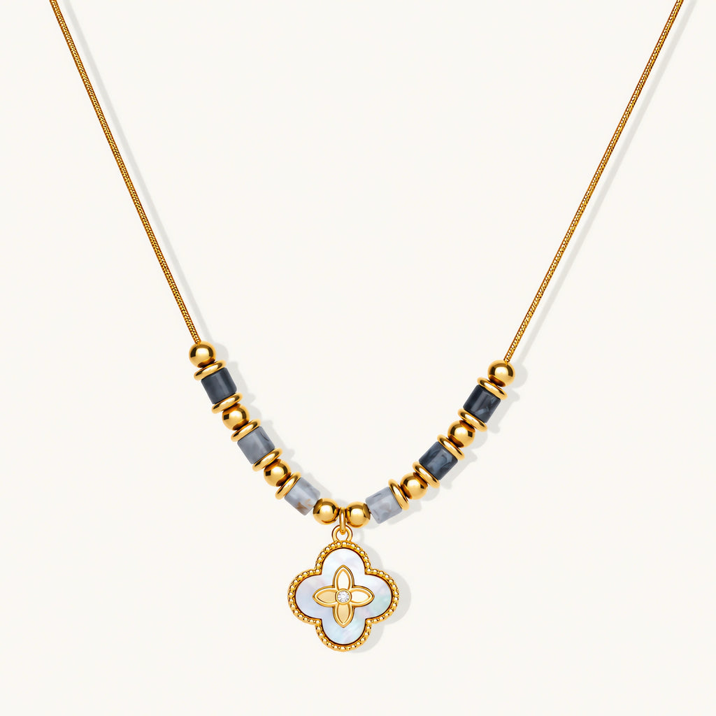 Gold-toned beaded necklace with grey stones and quatrefoil abalone shell pendant on cream background.