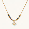 Gold-toned beaded necklace with grey stones and quatrefoil abalone shell pendant on cream background.