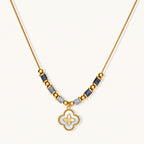 Gold-toned beaded necklace with grey stones and quatrefoil abalone shell pendant on cream background.