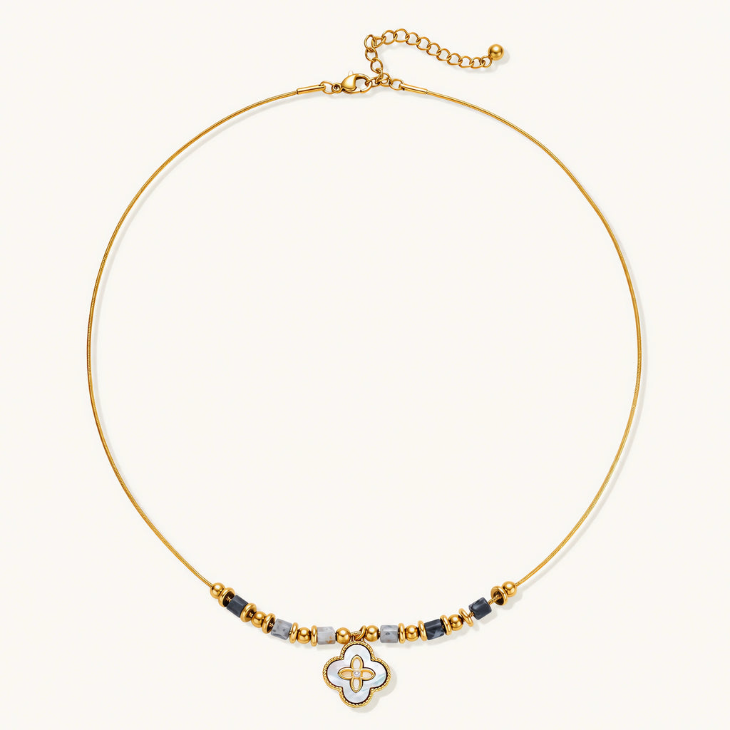 Gold-toned beaded necklace with grey stones and quatrefoil abalone shell pendant on cream background.