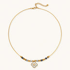 Gold-toned beaded necklace with grey stones and quatrefoil abalone shell pendant on cream background.