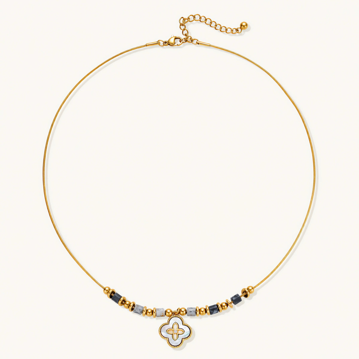 Gold-toned beaded necklace with grey stones and quatrefoil abalone shell pendant on cream background.